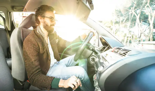 Young hipster fashion model driving car - Happy confident man with beard and alternative mustache smiling at business roadtrip - Lens flare halo as part of composition - Bright vintage filter
