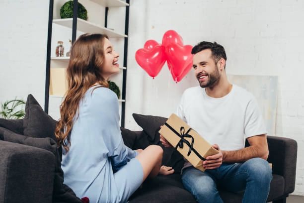 young man presenting gift box to girlfriend at valentines day young man presenting gift box to girlfriend at valentines day gift lounge stock pictures, royalty-free photos & images