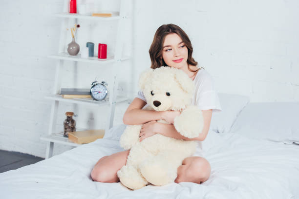 istock beautiful woman hugging teddy bear and sitting on bed with white bedding 1095482192