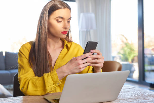 istock Young woman text messaging while sitting behind her laptop and working from home 1095489312