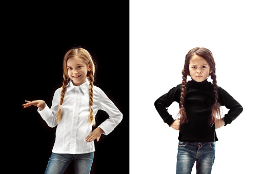 The portrait of two emotional happy surprised girl and serious angry girl on a white and black studio background. Human emotions concept. Comparison of different emotions. The childhood, kid, friendship concept