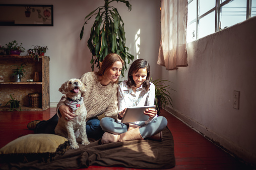Horizontal photo of mother and daughter using digital tablet at their cosy living room.