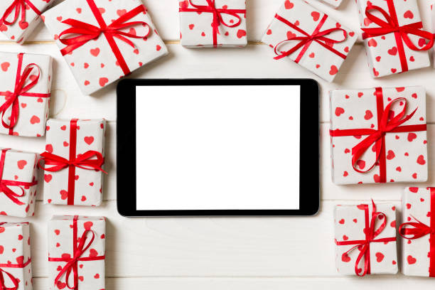 istock Digital tablet blank screen with gift box and hearts decor on wooden table. Top view. Valentines Day or other holidays concept background 1095508736