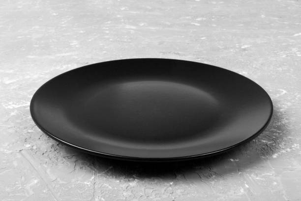 Top view of matte round empty black plate on grey cement background copy space for you design. Perspective view