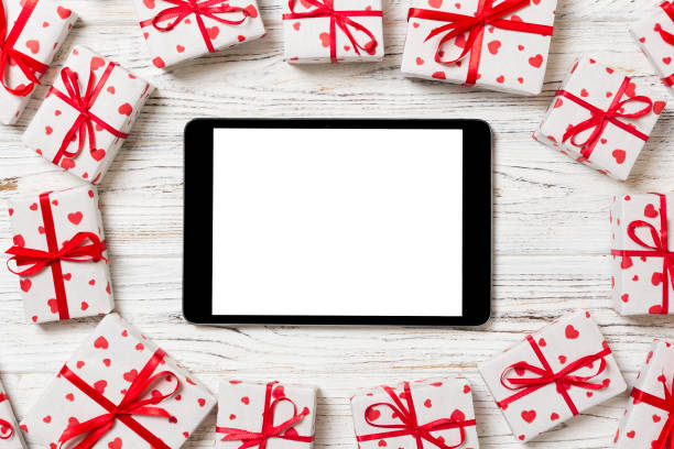 istock Digital tablet blank screen with gift box and hearts decor on wooden table. Top view. Valentines Day or other holidays concept background 1095513048