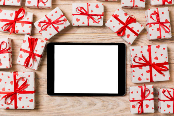 istock Digital tablet blank screen with gift box and hearts decor on wooden table. Top view. Valentines Day or other holidays concept background 1095513304