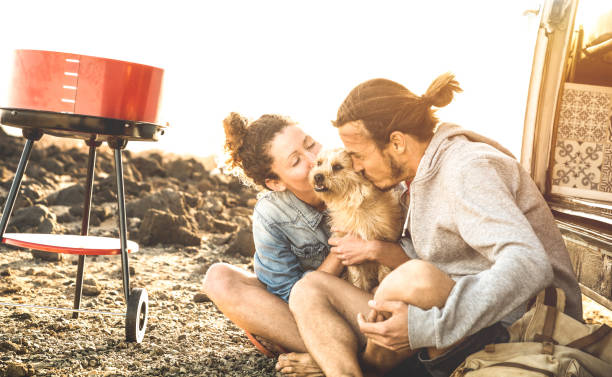 Hipster couple and cute dog relaxing by travel on oldtimer mini van transport - Wander lifestyle concept with indy people on minivan adventure trip having fun at barbecue moment - Warm sunshine filter Hipster couple and cute dog relaxing by travel on oldtimer mini van transport - Wander lifestyle concept with indy people on minivan adventure trip having fun at barbecue moment - Warm sunshine filter camper trailer photos stock pictures, royalty-free photos & images
