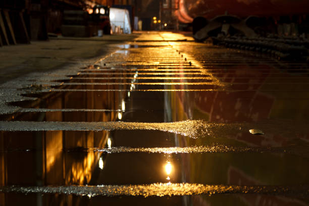 réflexions dans une flaque d’eau rouillée. faible éclairage ambiance industrielle. - construction built structure building activity shipyard photos et images de collection