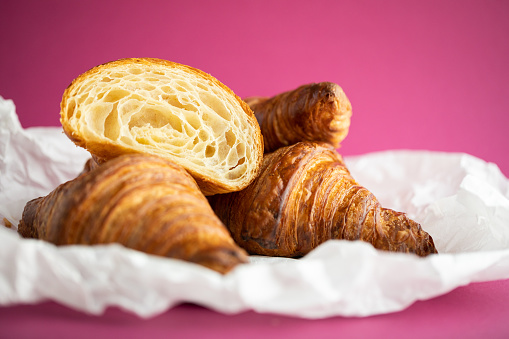 Fresh croissants on paper on pink background