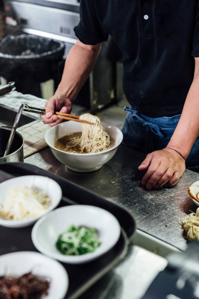 Chef making Hakata style Chashu Ramen by holding ramen noodle in Shio soup with chopsticks.