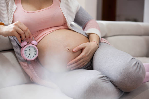 Soon mommy. regnant woman holds hands on belly and looking on an alarm clock. pregnancy and childbirth stock pictures, royalty-free photos & images