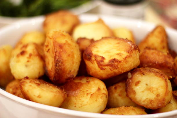 Crispy Golden Roast Potatoes White dish served with golden roast potatoes piled high on top of each other. Out-of-focus background. Landscape orientation. crunchy photos stock pictures, royalty-free photos & images