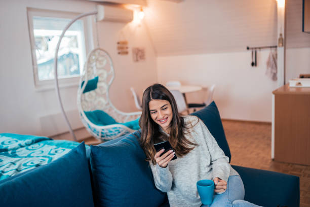 istock Happy young woman using smart phone while sitting on the sofa at cozy apartment. 1095552844