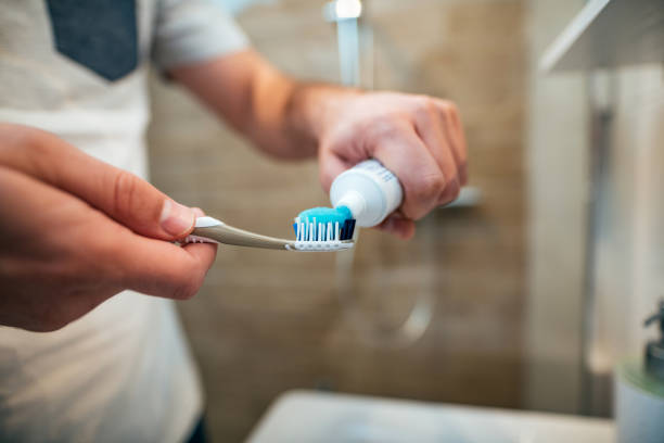 歯科医療の概念。男のクローズ アップは、歯ブラシに歯磨き粉を圧縮します。 - toothpaste ストックフォトと画像