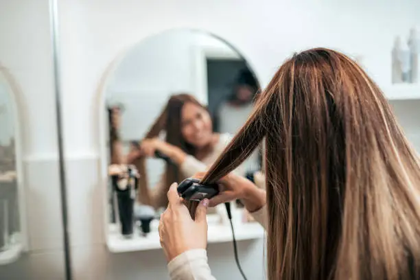Rear view of young woman straightening hair with straightener.