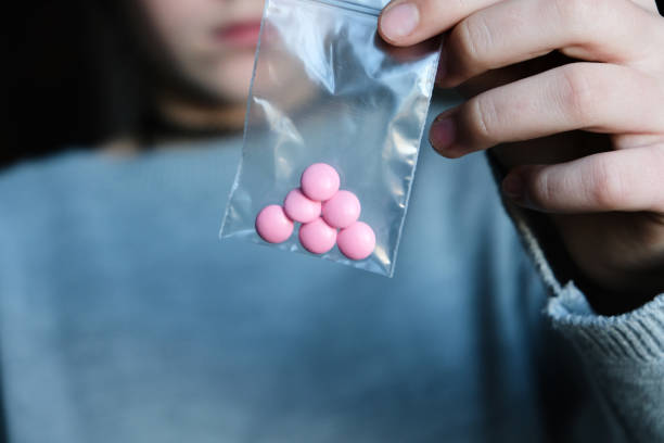 Woman holding in her hand pink pills in a little plastic bag zipper. Drugs, medecine, narcotik Woman holding in her hand pink pills in a little plastic bag zipper. Drugs, medecine, narcotik over a grey background. narcotic stock pictures, royalty-free photos & images