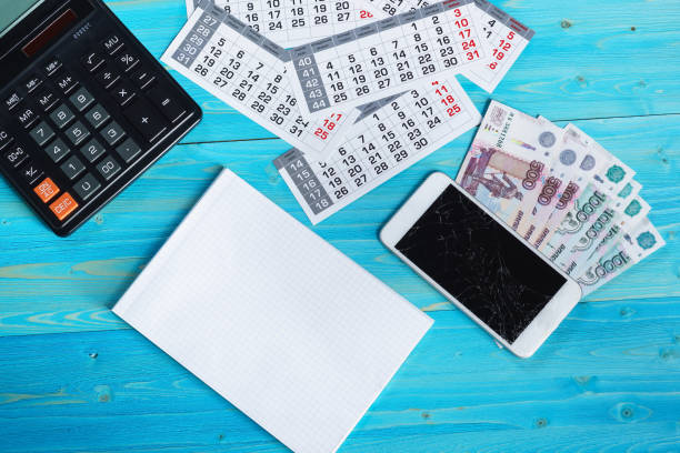 istock Calendar, clean notebook, broken smartphone and Russian money on a blue wooden table 1095576148