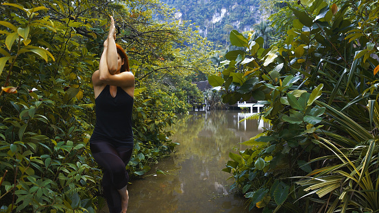 Young woman practicing yoga on a pier. River in the jungle