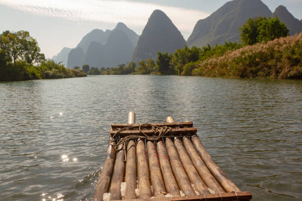 Front of bamboo raft in foreground on Yulong River, Yangshuo, China. Limestone cliffs in silhouette along edge of river.