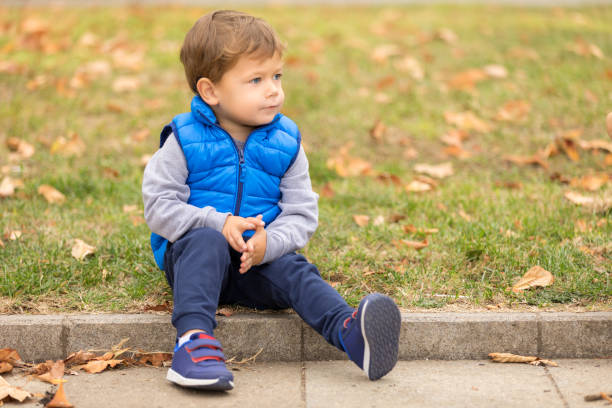 Boy In A Blue Vest Sitting On A Curb In The Park