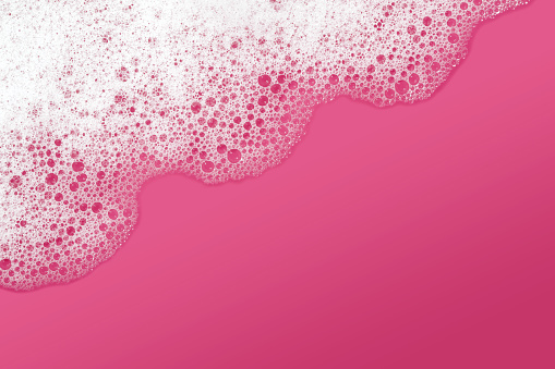Close-up of soap sud with water on a pink background. Space for copy.
