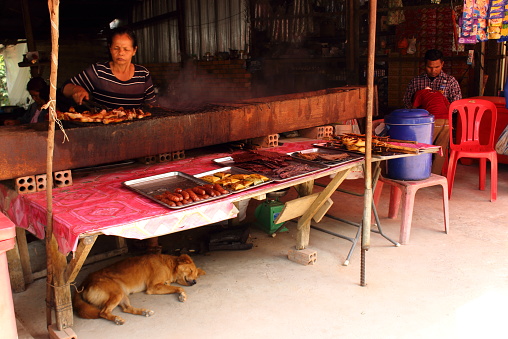 SIEM REAP, CAMBODIA - Mart 25, 2018: Unhurried cambodian life. Cooking local cuisine on grill and barbecue for tourists on the counter and travelers of a street food vendor in Cambodia.