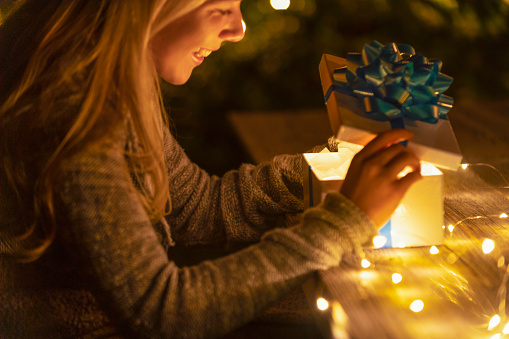 Woman opening a gift box. There is a glow coming from the box. There is a rustic wood table underneath her hands. Valentines day, Christmas or anniversary concept. Copy space.