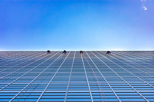 Four window washers cleaning on the side of a modern glass skyscraper in a city