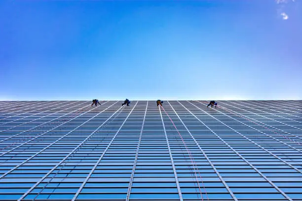 Four window washers cleaning on the side of a modern glass skyscraper in a city