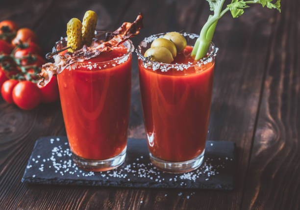 Two glasses of Bloody Mary Two glasses of Bloody Mary garnished with gherkins, fried bacon strips, green olives and celery stalk bloody mary stock pictures, royalty-free photos & images