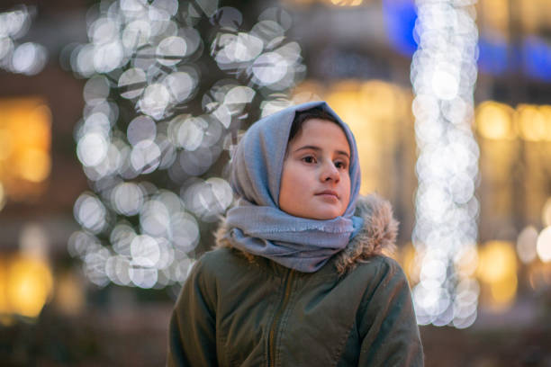 A beautiful Muslim girl stands outside on a cold winter day. She is looking off into the distance with a stoic look on her face.