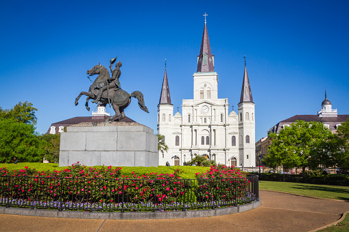 St. Louis Cathedral, Jackson Square, Louisiana, United States. Color horizontal image with Andrew Jackson statue in foreground with red flowers.