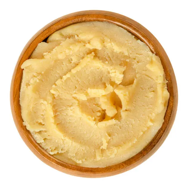 Yellow marzipan paste in wooden bowl. Marzapana or marchpana, made of ground almonds and sugar or honey. Used for sweets and to shape small figures. Food photo closeup from above, on white background.