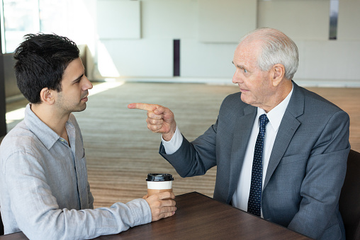 Senior businessman blaming his employee. Entrepreneur pointing at young coworker. Argument concept