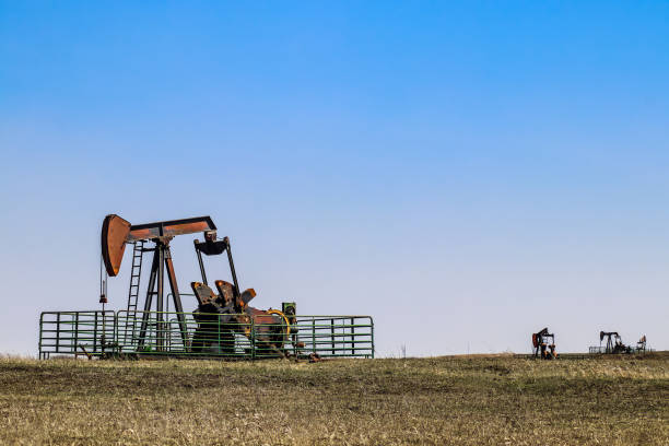quattro pumpjack che estraggono petrolio o gas all'orizzonte di un campo invernale sotto il cielo blu - oil pump oil industry prairie field foto e immagini stock