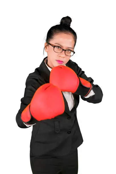 Asian businesswoman ready to fight while wearing boxing gloves and standing in the studio, isolated on white background