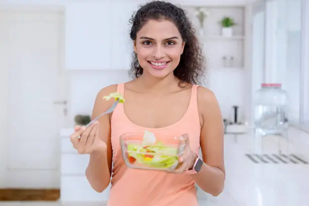 Portrait of beautiful woman eating a bowl of fresh salad while standing in the kitchen