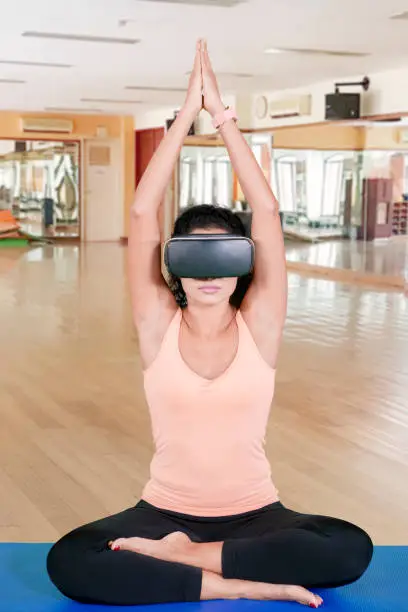 Young Indian woman meditating in the fitness center while wearing virtual reality glasses