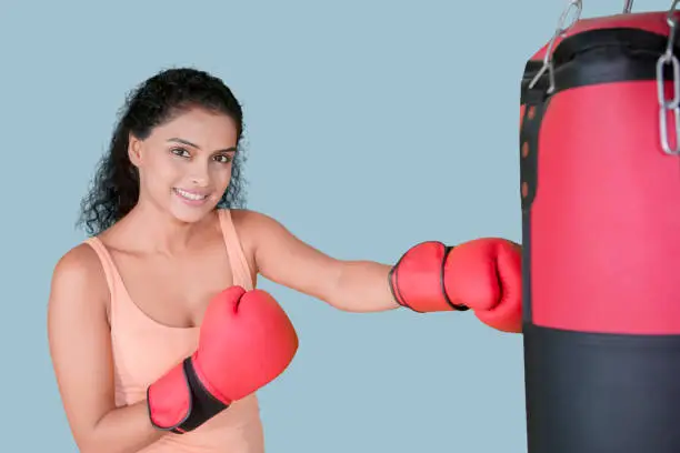 Picture of pretty girl smiling at the camera while punching a boxing bag in the studio