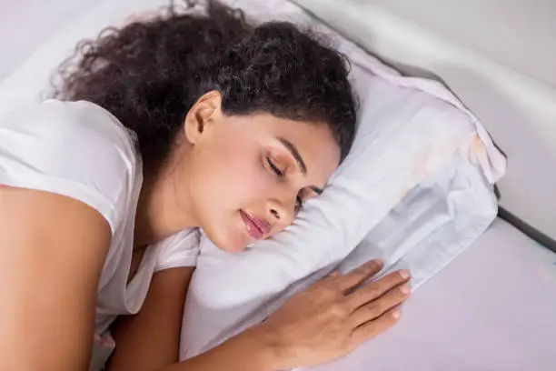 Close up of young Indian woman is resting in bed with eyes closed. Shot in the bedroom