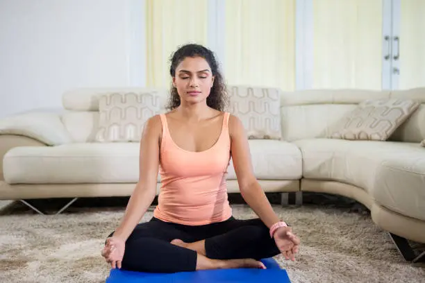 Picture of pretty girl wearing sportswear while doing meditation in the living room. Shot at home