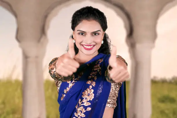 Picture of young Indian woman smiling at the camera while showing thumbs up at home