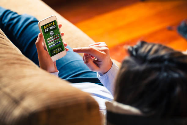 Mobile phone with sports betting website app in the screen. Woman holding a mobile phone to visit a sports betting website while lies down at home. sports betting stock pictures, royalty-free photos & images