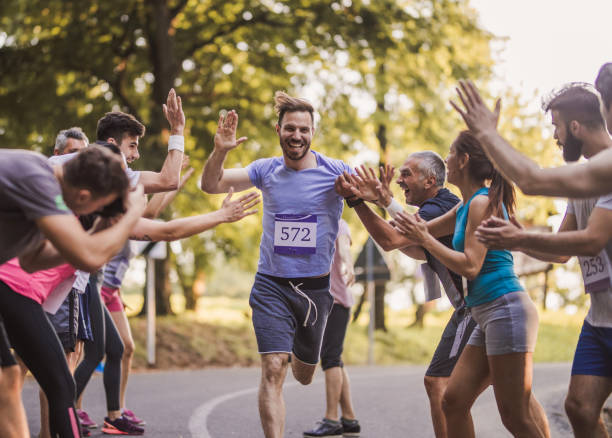Cheerful marathon runner greeting group of athletes at finish line. Young happy man greeting with group of supporters at finish line after marathon race. marathon stock pictures, royalty-free photos & images