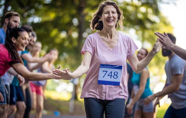 幸せの年配の女性マラソンを仕上げ、支持者のグループとの挨拶します。 - marathon running group of people jogging ストックフォトと画像