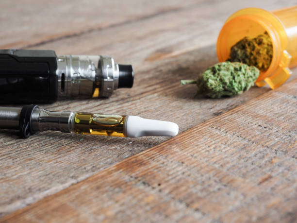 Close Up Shot Of Real Cannabis Or Weed With Cannabis Oil In Cartridge Of  Vape Pen In The Foreground Shot On Wooden Floor With Text Space On The  Right Stock Photo -
