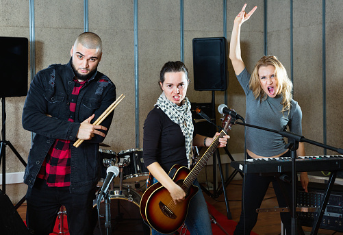 Three happy positive  bandmates posing together with musical instruments in rehearsal room
