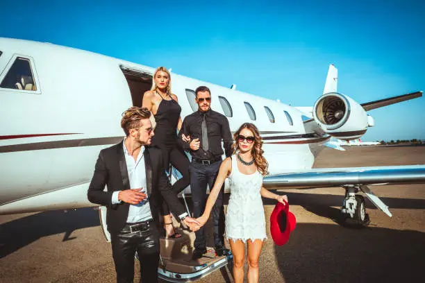 Two rich and famous couples exiting a private airplane parked on an airport taxiway.