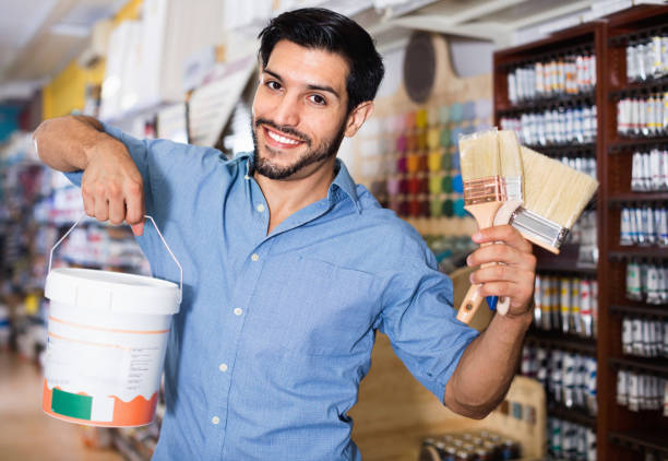 istock Man standing amongst racks in paint store with brushes and paint 1095871982