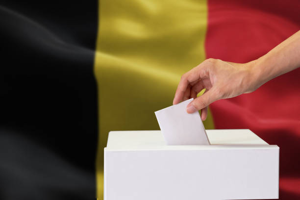 istock Close-up of human hand casting and inserting a vote and choosing and making a decision what he wants in polling box with Belgium flag blended in background. 1095879256